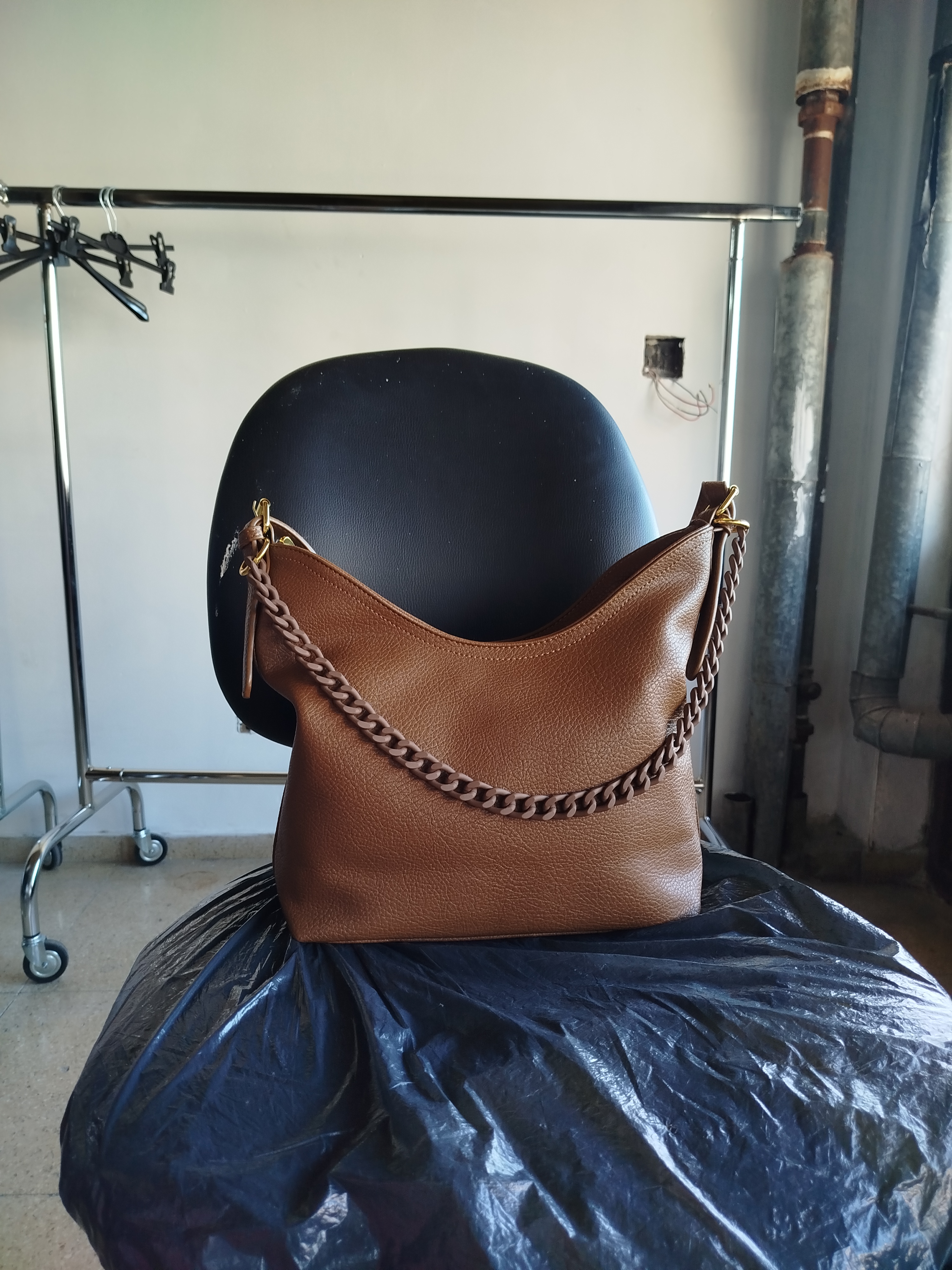 Bolso hobo de cuero marrón apoyado sobre una silla en el taller