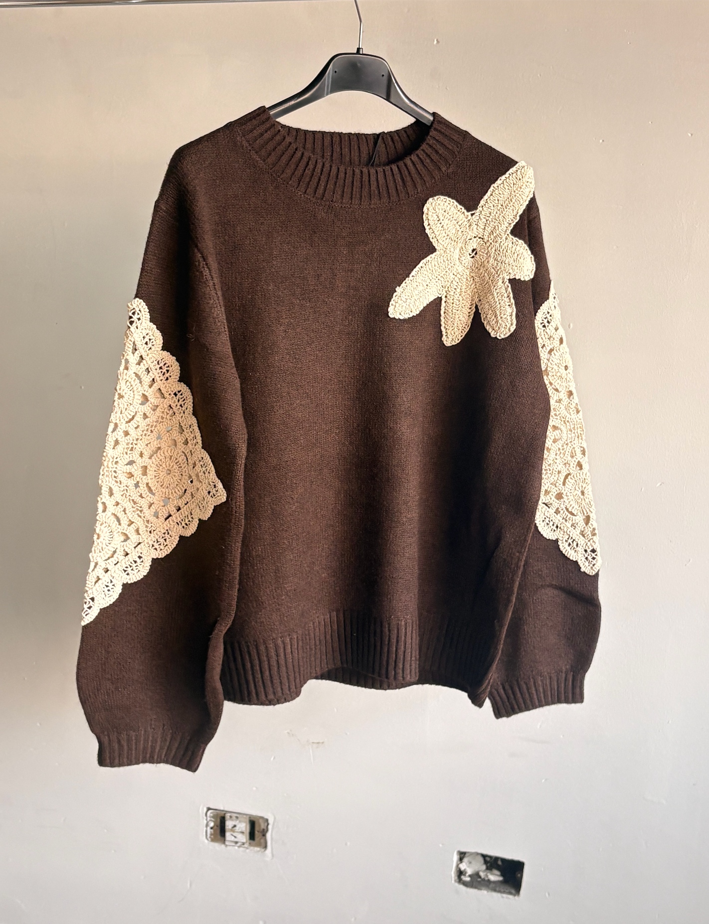 Sweater marrón con apliques de crochet colgado de una percha en el taller