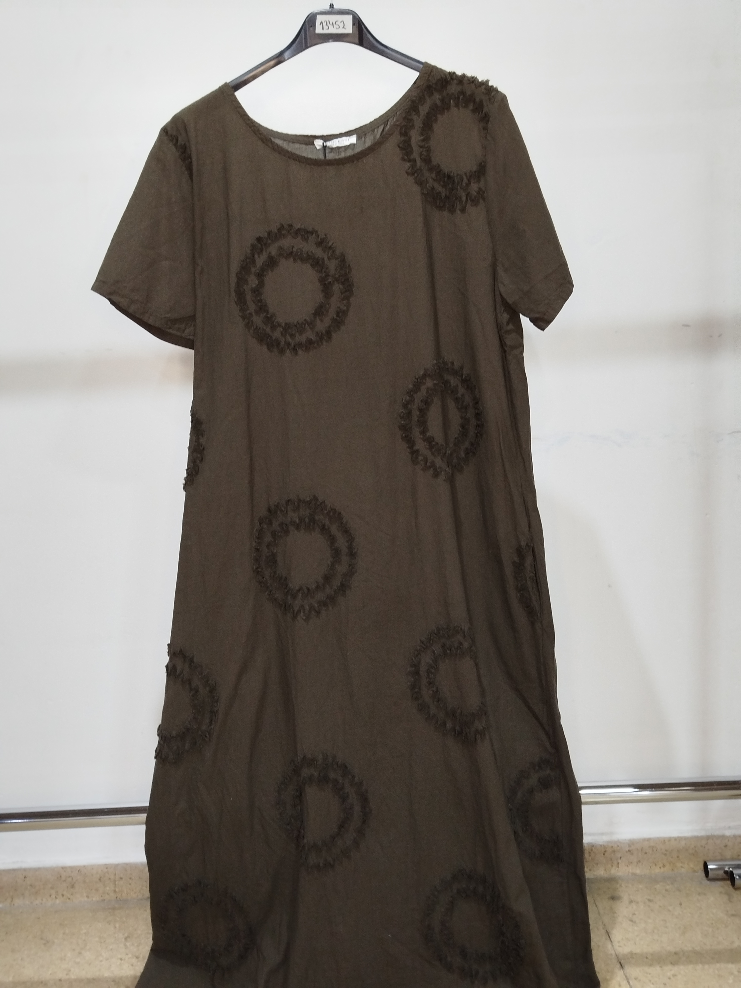 Vestido de lino verde oliva fotografiado en percha contra la pared del depósito